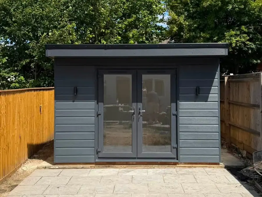 The finished garden room, clad in grey boards with glazed double doors, on a new paved patio