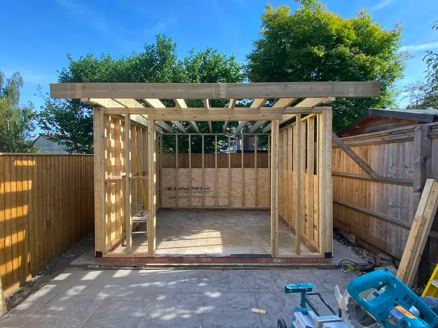The same garden room at bare timber-frame stage against a blue sky