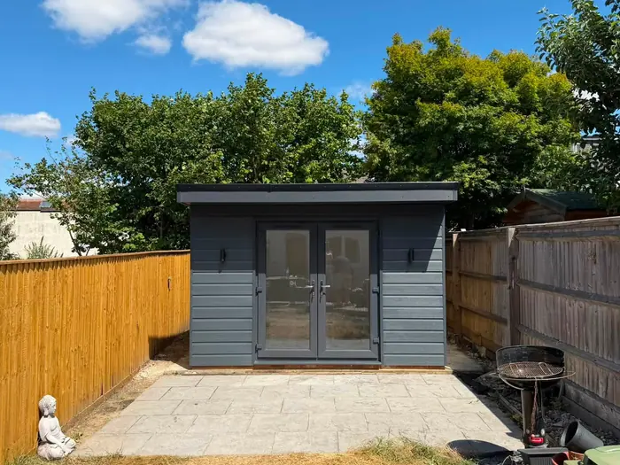 Finished grey-clad garden room with dark doors on a gravelled plot