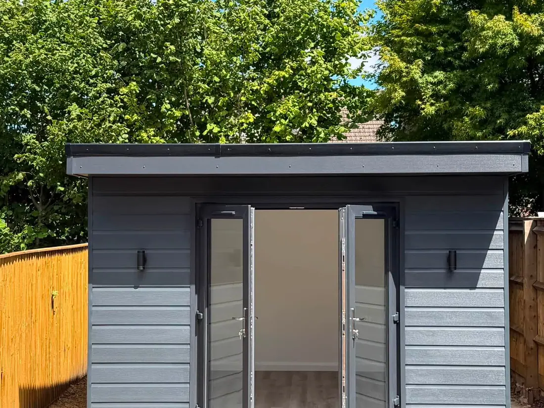 Completed garden room clad in grey boards with anthracite bifold doors open onto a patio