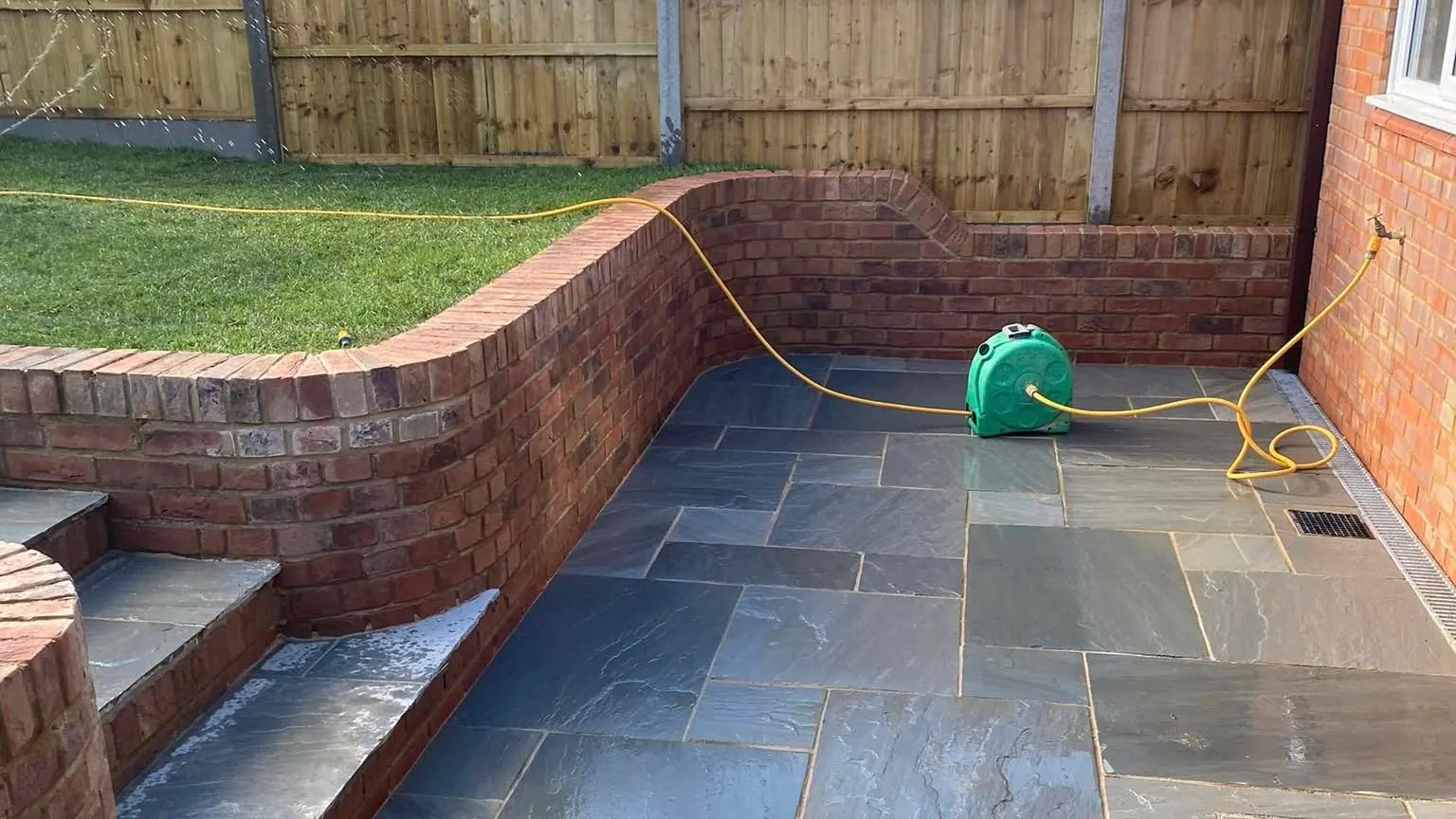A finished garden with a curved red-brick retaining wall and a slate patio