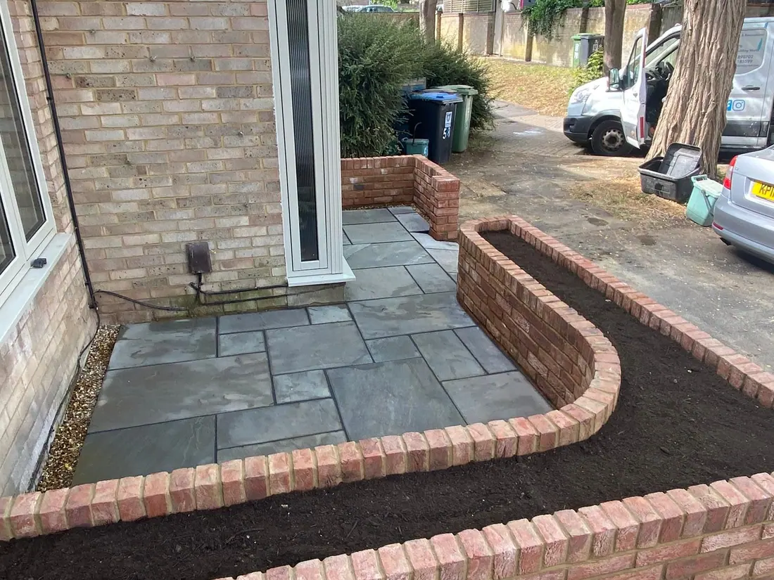 Sandstone paving curving around a red-brick planter beside a house